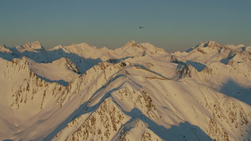 Helicopter flies quickly over snow covered mountain range and hollows full of shadows