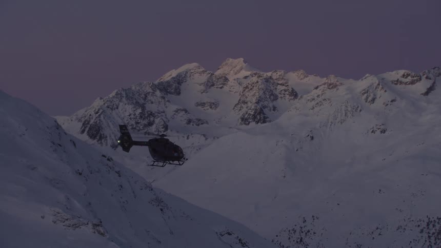 Helicopter flies along valley between snow covered mountains