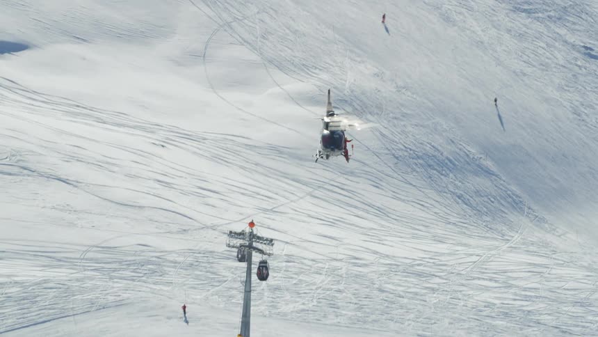 A helicopter flying over a snowy slope with people skiing
