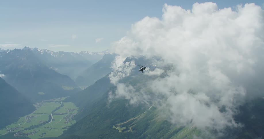 A helicopter flies into dense clouds as it passes over a canyon