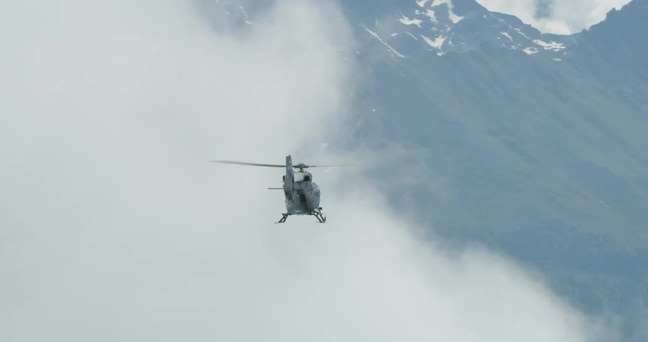 Helicopter flies through clouds to emerge over mist covered mountain and valley