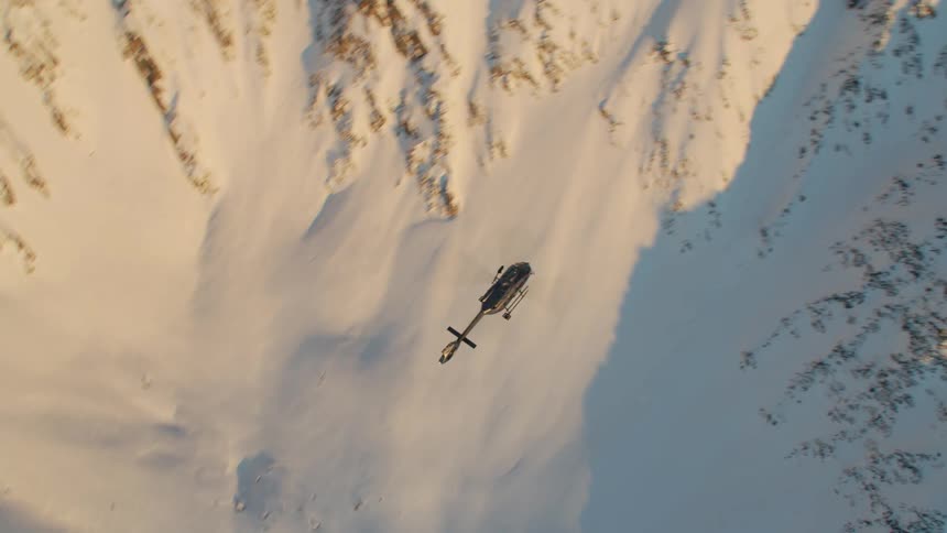 A helicopter flying over snowy mountains in winter