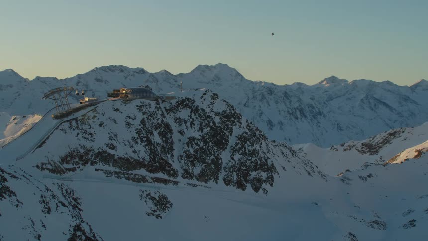 A helicopter flying over a snow covered mountain range with the sky and clouds in the background