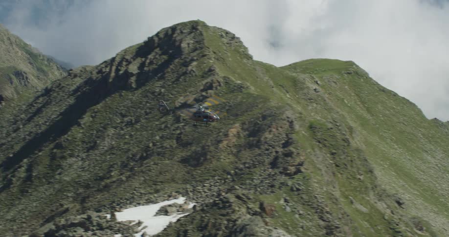 A helicopter flying over green rocky ridges