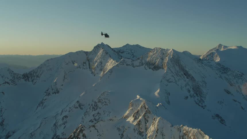 A helicopter flying over a snow covered mountain range with the sky and clouds in the background