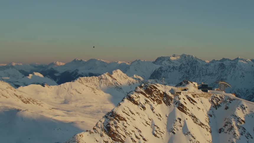 A helicopter flying over a snow covered mountain range with the sky and clouds in the background