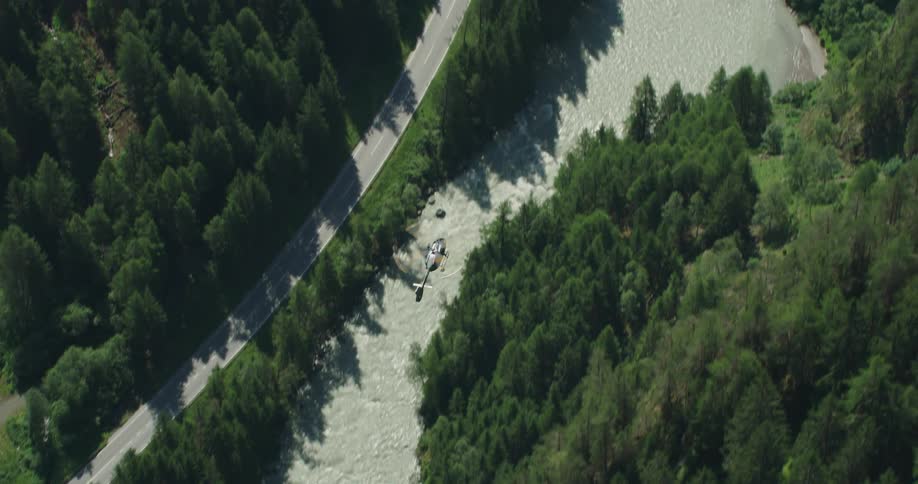 A helicopter flies over a dense forest and rural highway