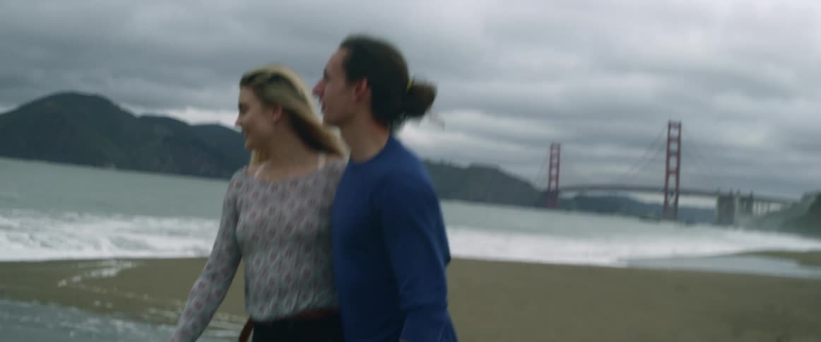 A man and woman walk along the beach and she hugs him