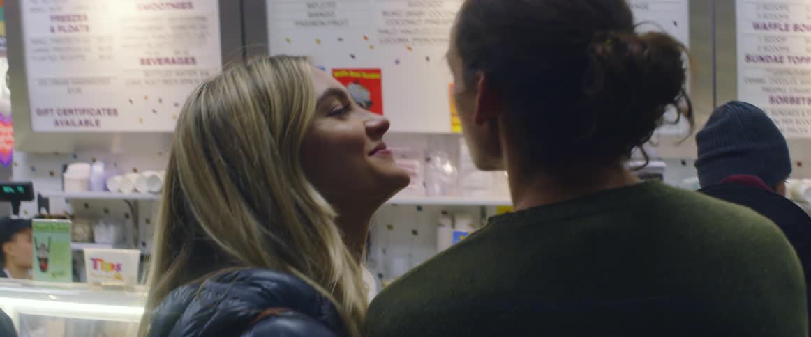 A man and woman kiss as they stand in an ice cream shop