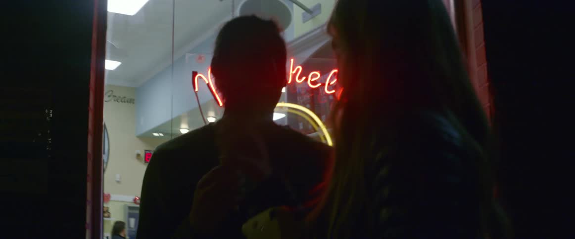 A man and woman look at a photograph in front of a shop at night
