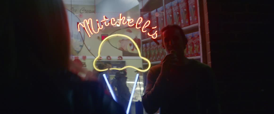 A woman photographing a man holding an ice cream cone in front of an ice cream shop