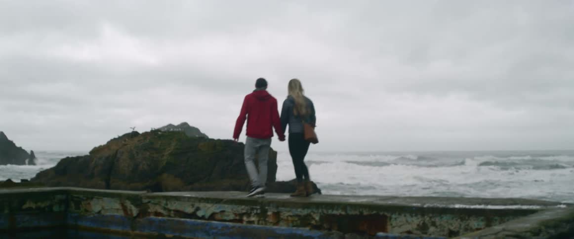 A man and woman walk along the shore on a cloudy day