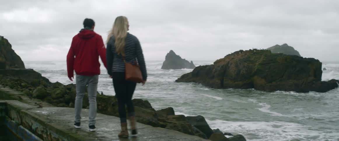 A man and woman hold hands walking by the water and hug