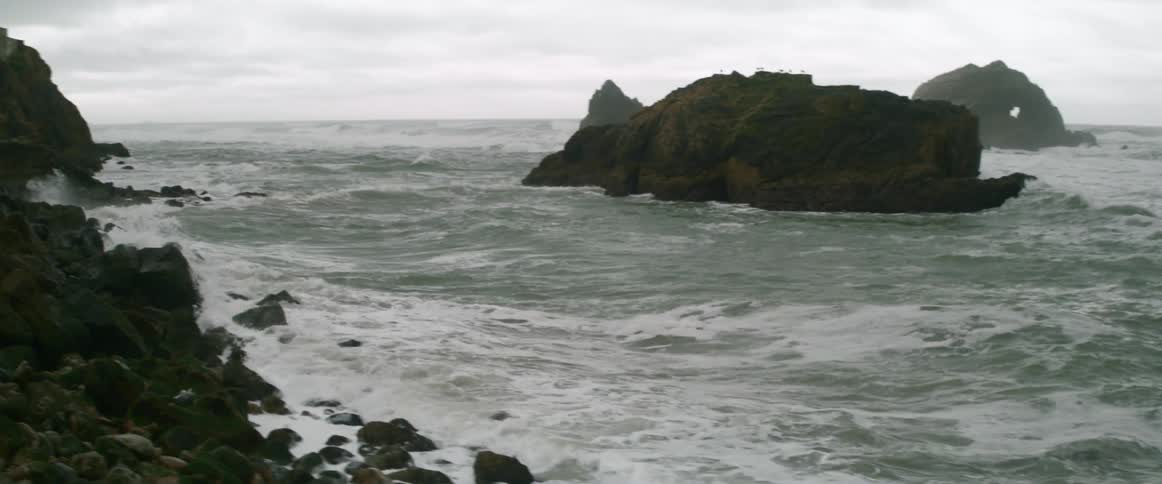Waves crash against the rocks on a cloudy day