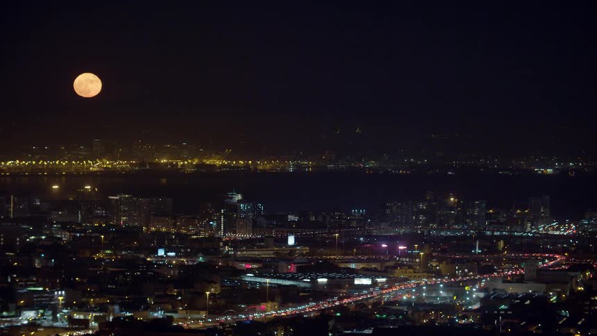 A yellow moon sits above a city at night