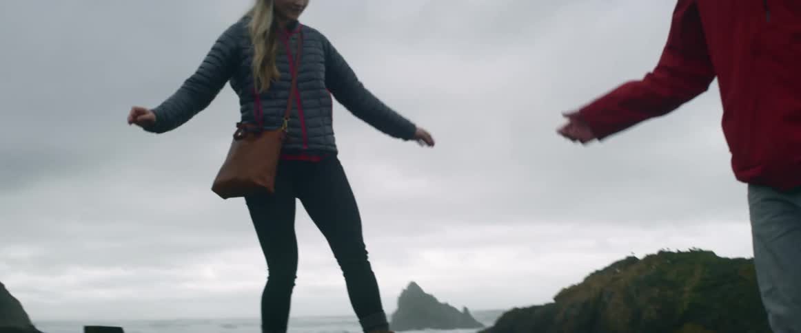 Two people are climbing over rocks on a shore