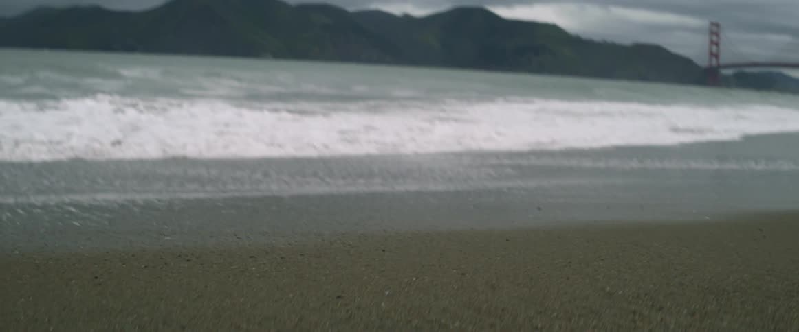 Waves move along the sand with a bridge ahead