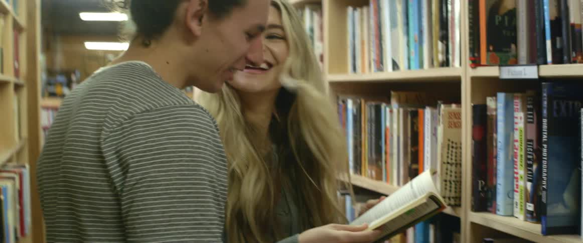A man and woman laugh as they browse a book in a library