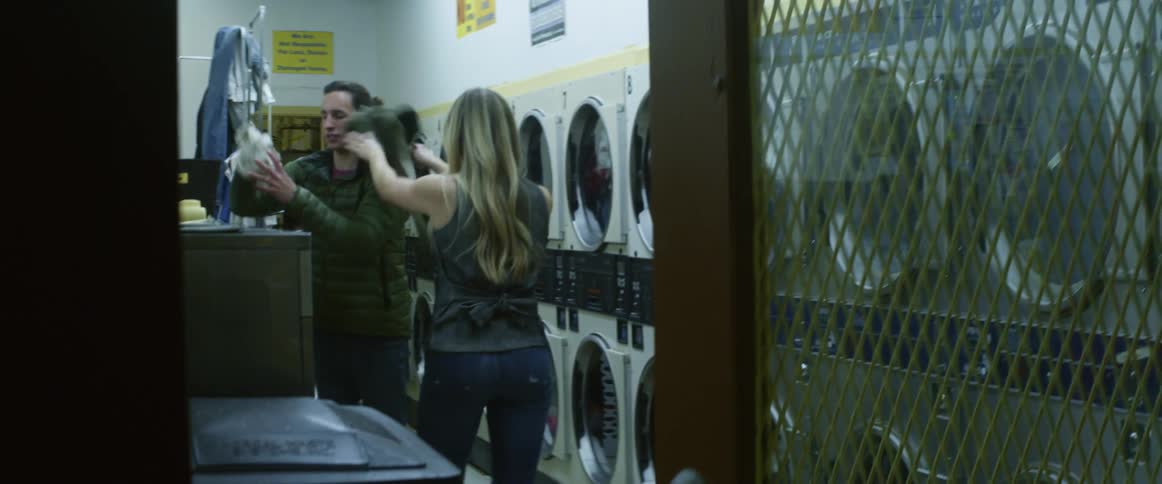 A woman playfully throws a shirt at a man while they do laundry at a laundromat