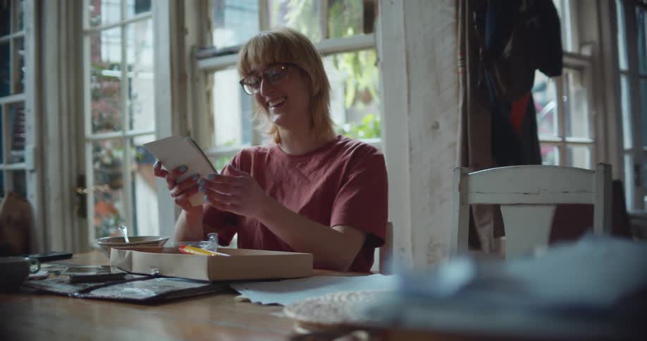 Blonde woman wearing glasses sits at table laughing and smiling while looking through photographs