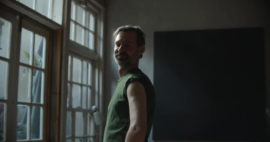A man stands in front of a bank of windows in a dark room and smiles
