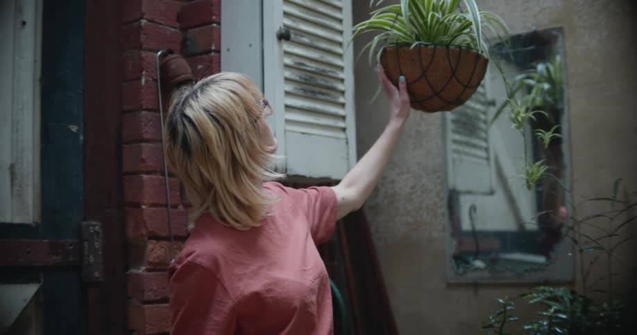 A woman checks a hanging plant in a room filled with plants