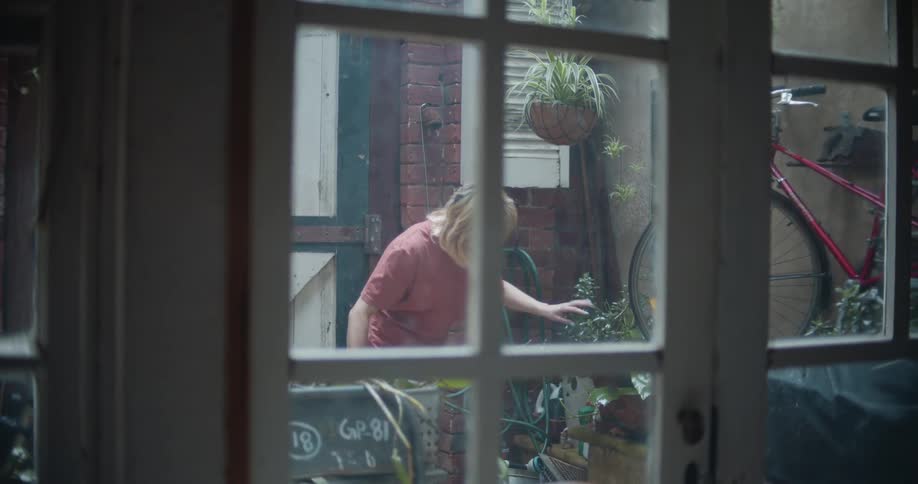 Blonde woman watering plants in a small apartment garden