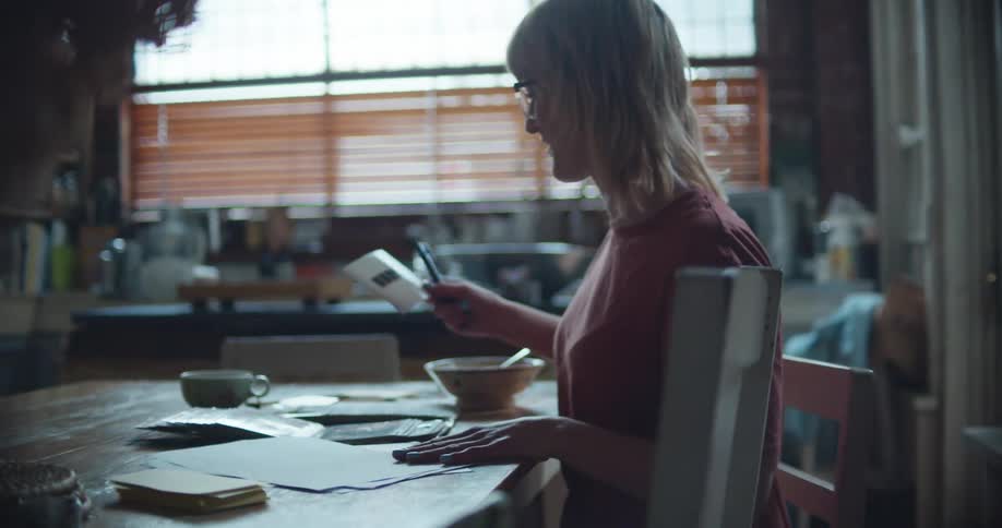Woman sits at a desk and looks through a photo album then removes a photo and refers to a file folder