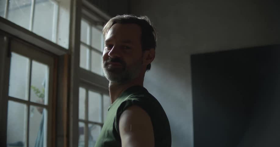 Bearded young man stainding in a dimly lit room looking at the camera