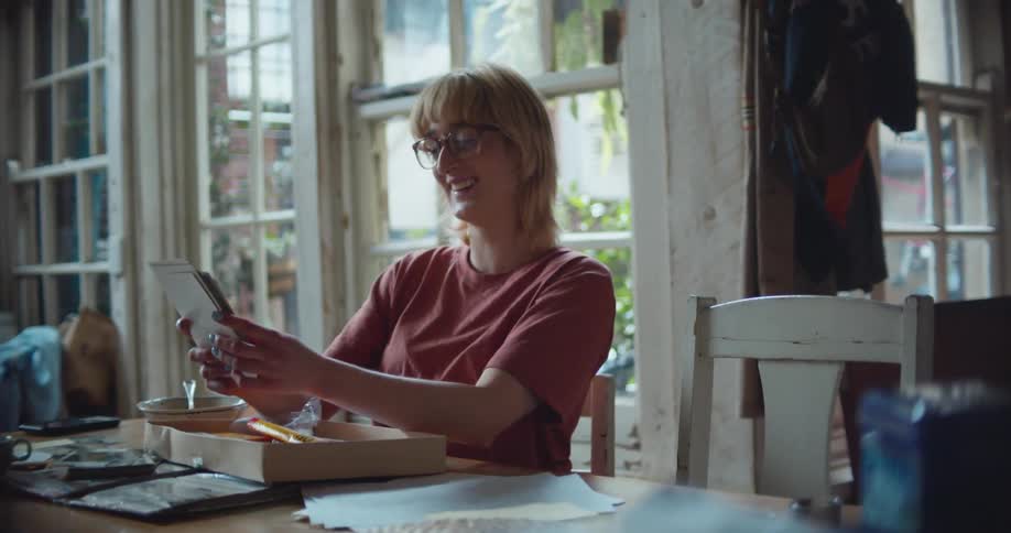 A blonde woman laughing while looking at pictures at a home dining table