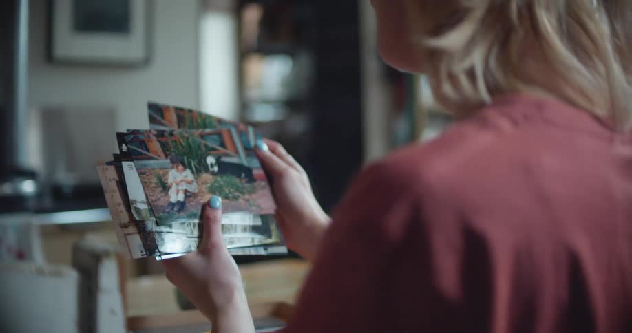 A woman looking through photographs while sitting at a home dining table