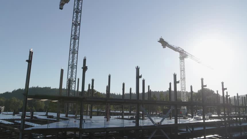 The sun shines down on steel beams and girders at the top of a new building under construction