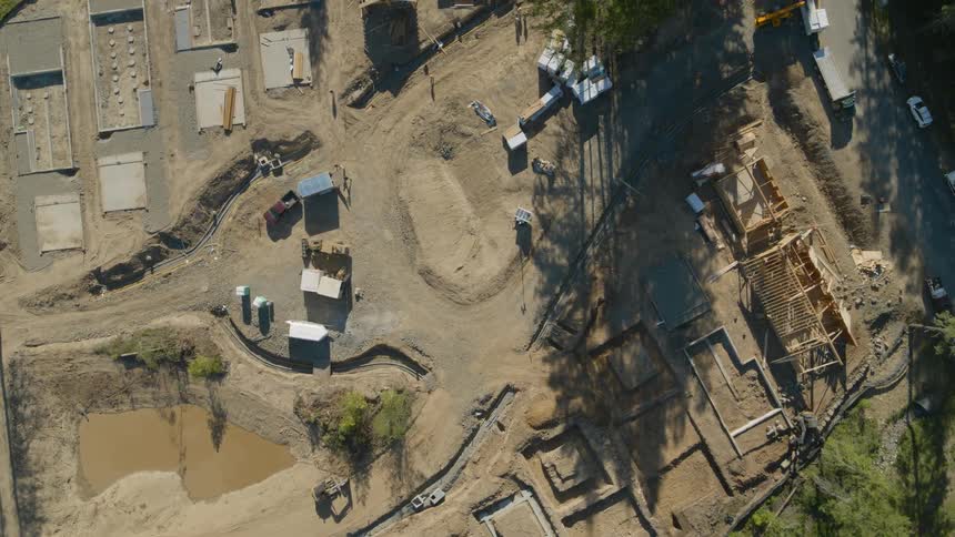 Birds eye view of a new residential construction project with freshly poured foundations and the early stages of wood framed homes
