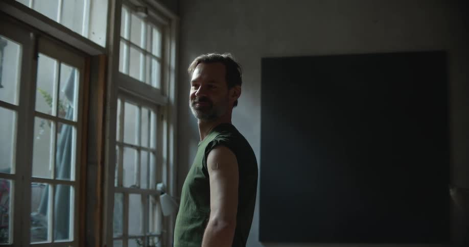 A man standing and staring in a room with a door window and a wall in the background