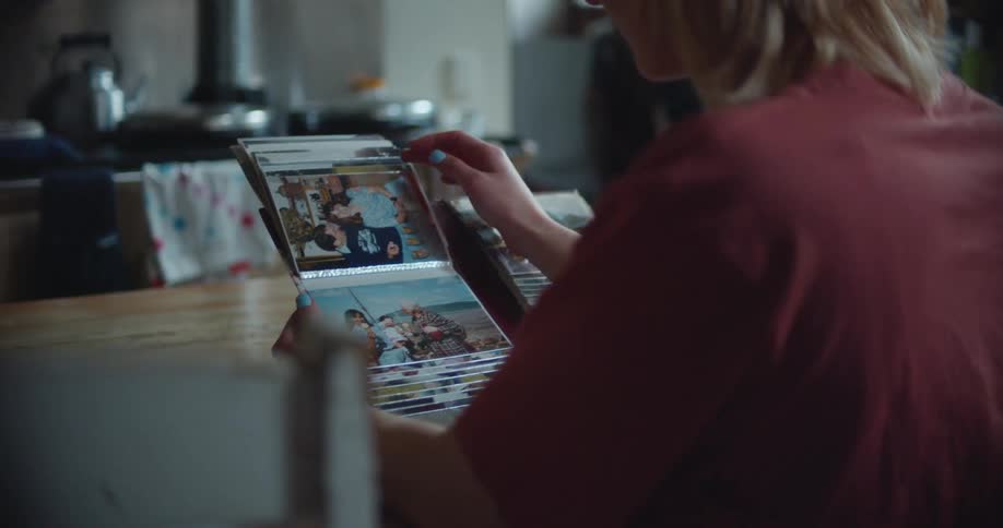 A woman in a room with glasses sitting at a desk looking at a photo album
