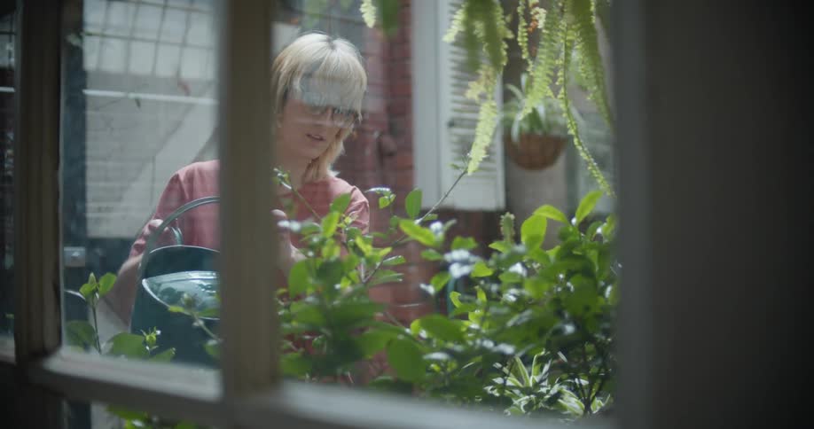 Woman uses a watering can to water a garden of green foliage