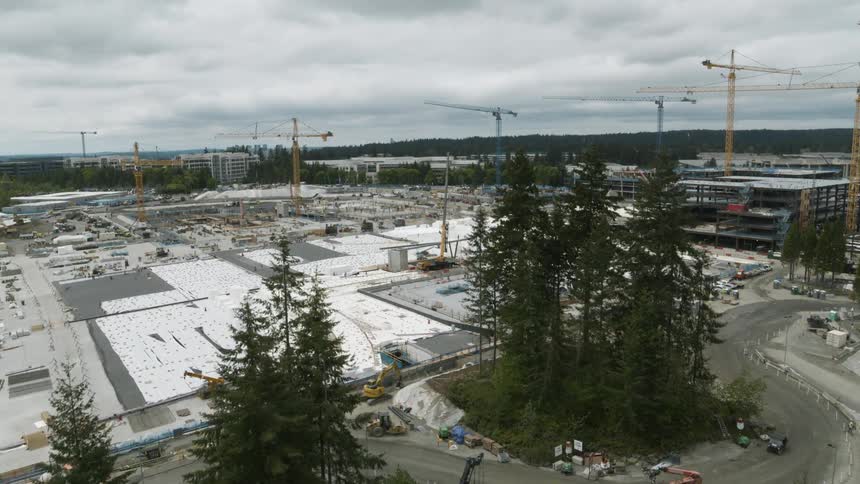 Reveal of a massive construction site complex from behind a stand of fir trees