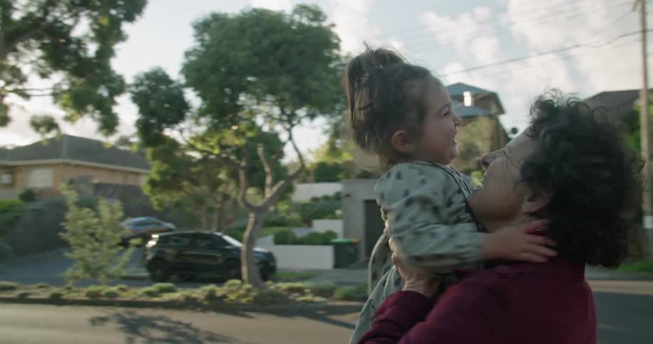 Young toddler jumps into her grandmothers arms and the grandmother spins around and kisses the little girl