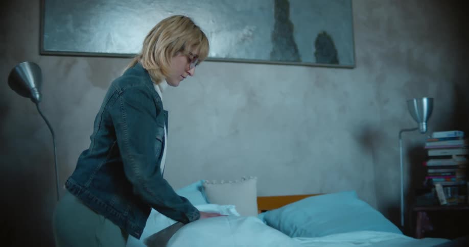 A woman carefully fluffs pillows as she remakes a large bed
