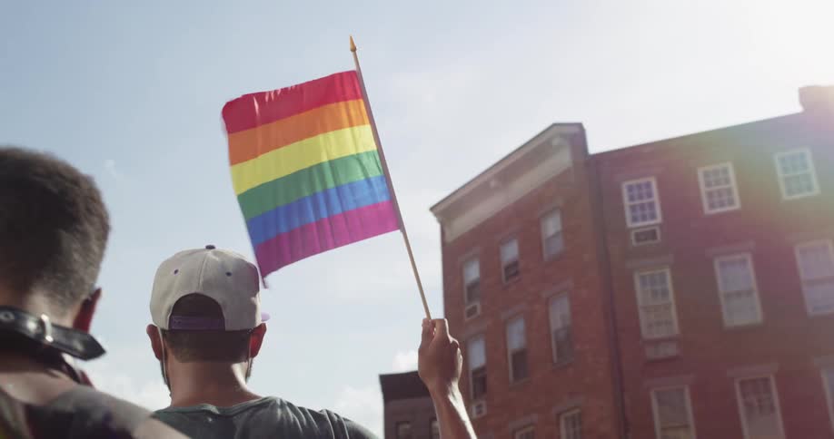Men walk as part of lgbt rainbow rally past apartment building under clear sky on a sunny day