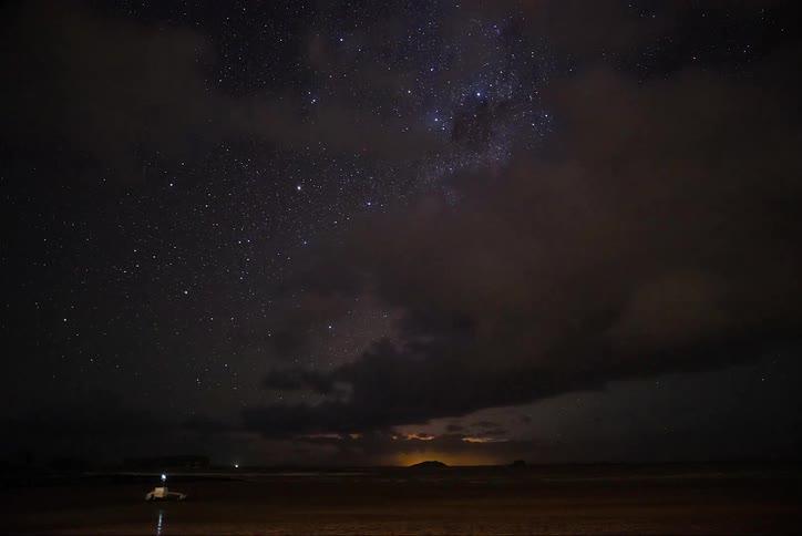 Clouds speed across the starry sky as the sun rises over a mountain