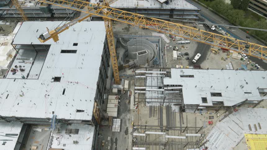 Traverse over multiple tower cranes working above the framework of new buildings under construction at an office park