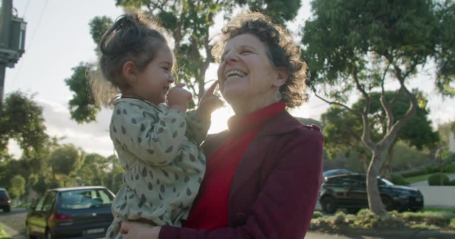 An elderly woman laughs while carrying a young girl in her arms