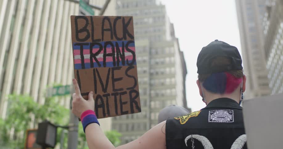 Protesters carrying signs walk through city downtown passing corner street sign
