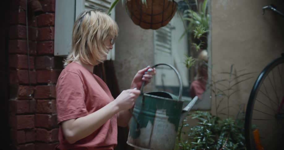 A woman is watering plants in a room with a metal watering can