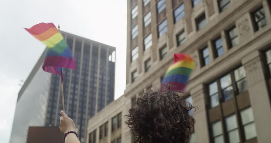 People march through city waving rainbow flags under cloudy sky