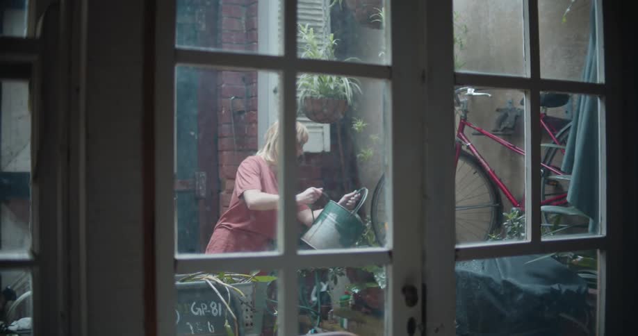 A woman in a garden watering plants with a wall and a door in the background