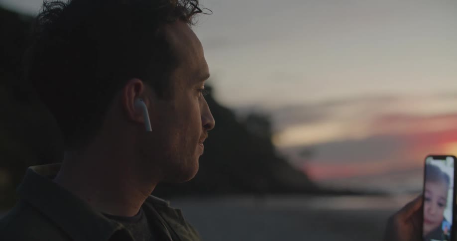 A man talks with a child on the phone as the sun sets on the beach