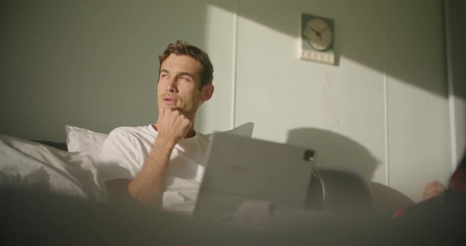 A man in a room sitting on a couch and using a laptop with a wall in the background