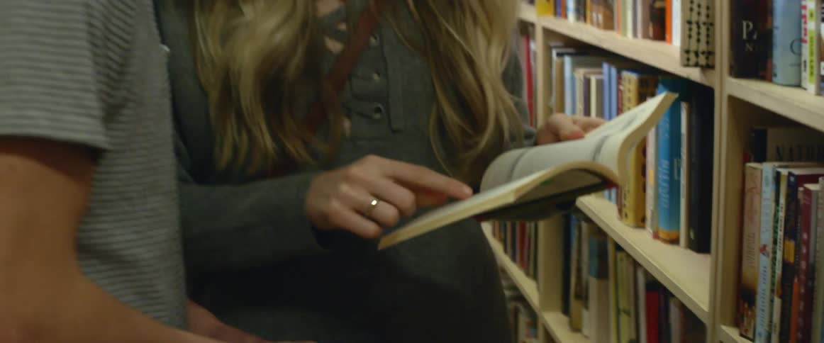 A man and woman examine books in a library talking